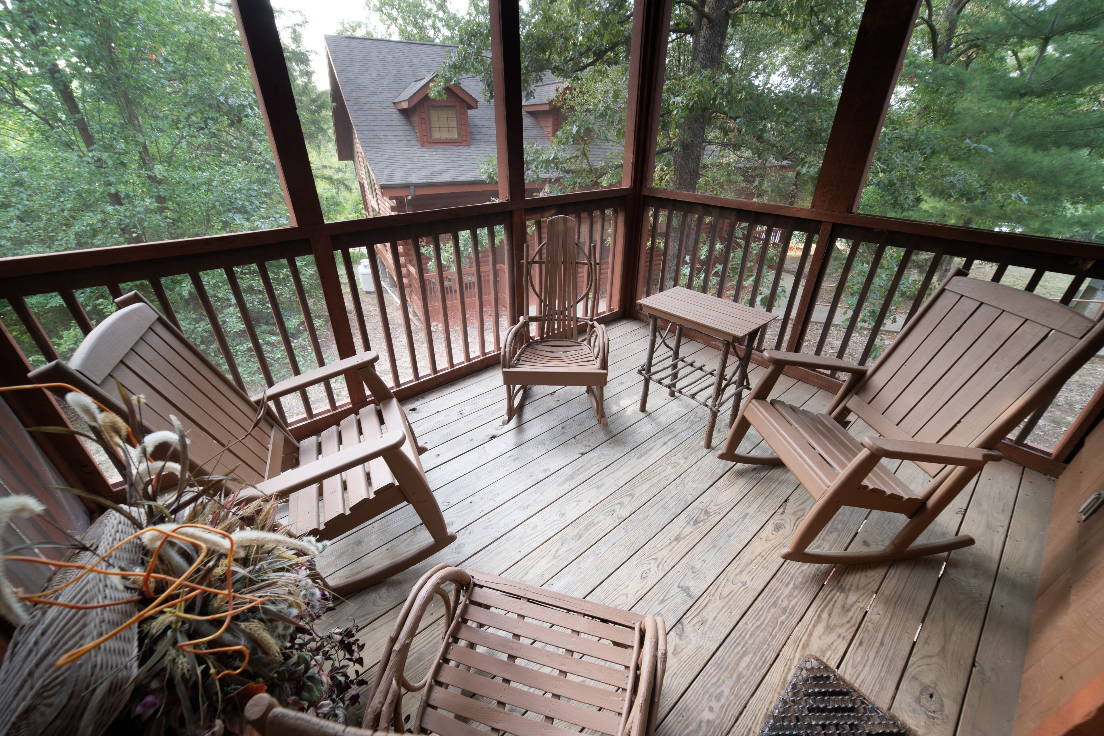 A wooden deck with four rocking chairs and a small table, surrounded by a wooden railing.