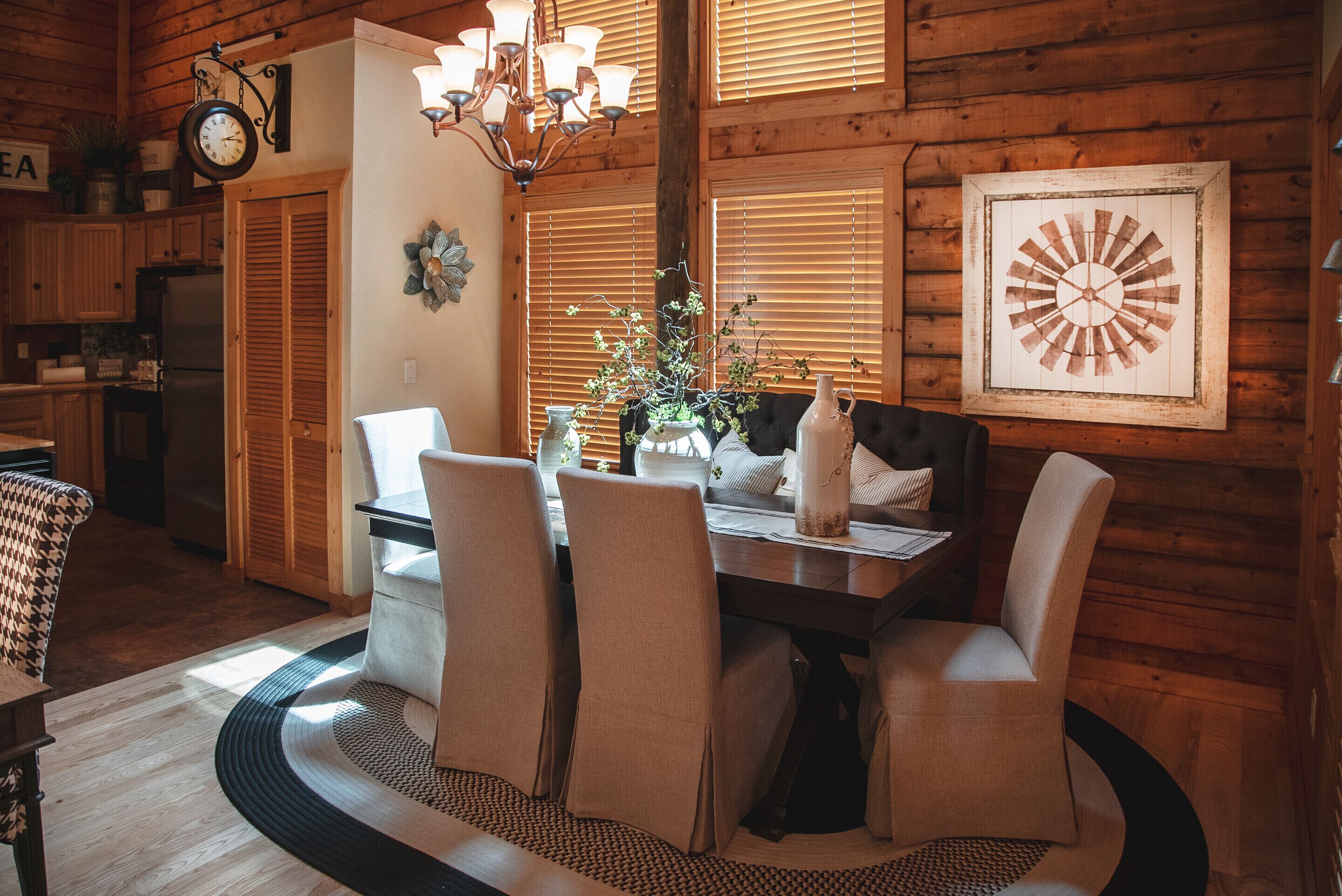 A dining area with a wooden table, four chairs, a chandelier, and a clock on the wall.