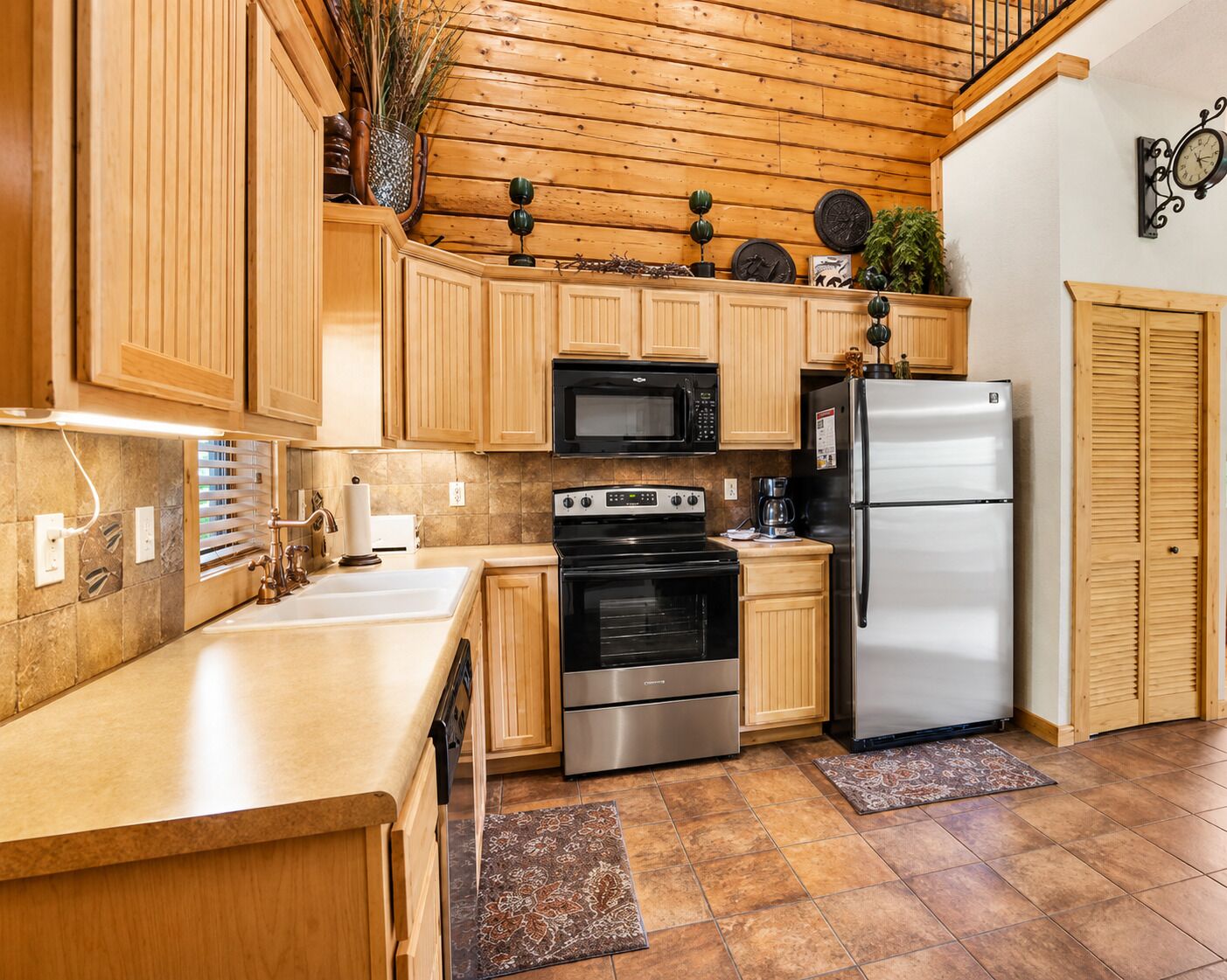 Una cocina con armarios de madera, un refrigerador de acero inoxidable, un microondas, un horno y un lavamanos.