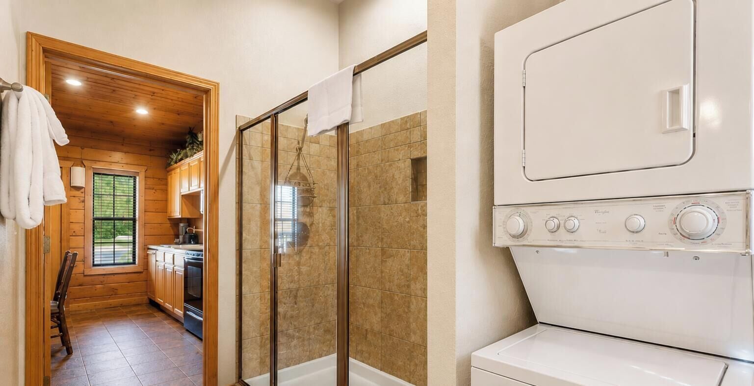 A laundry room with a glass-enclosed shower, a washing machine, and wooden cabinetry.