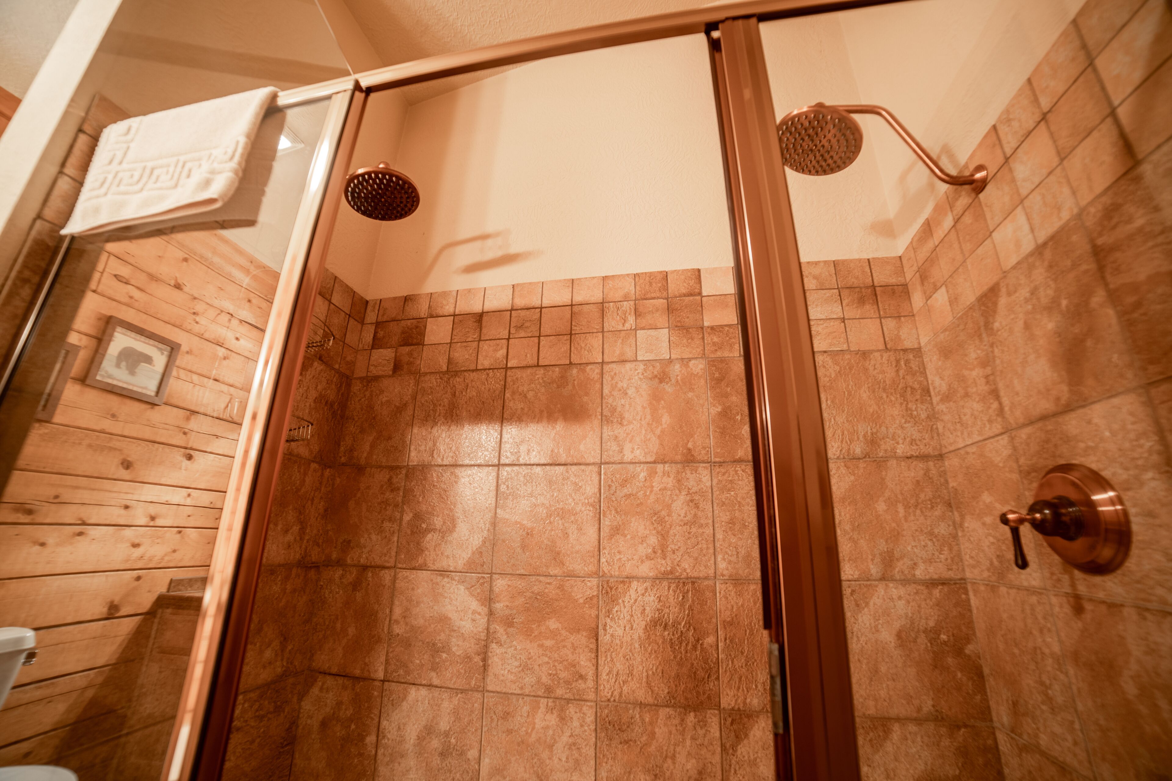 A shower area with a glass door, tiled walls, and a wooden floor.