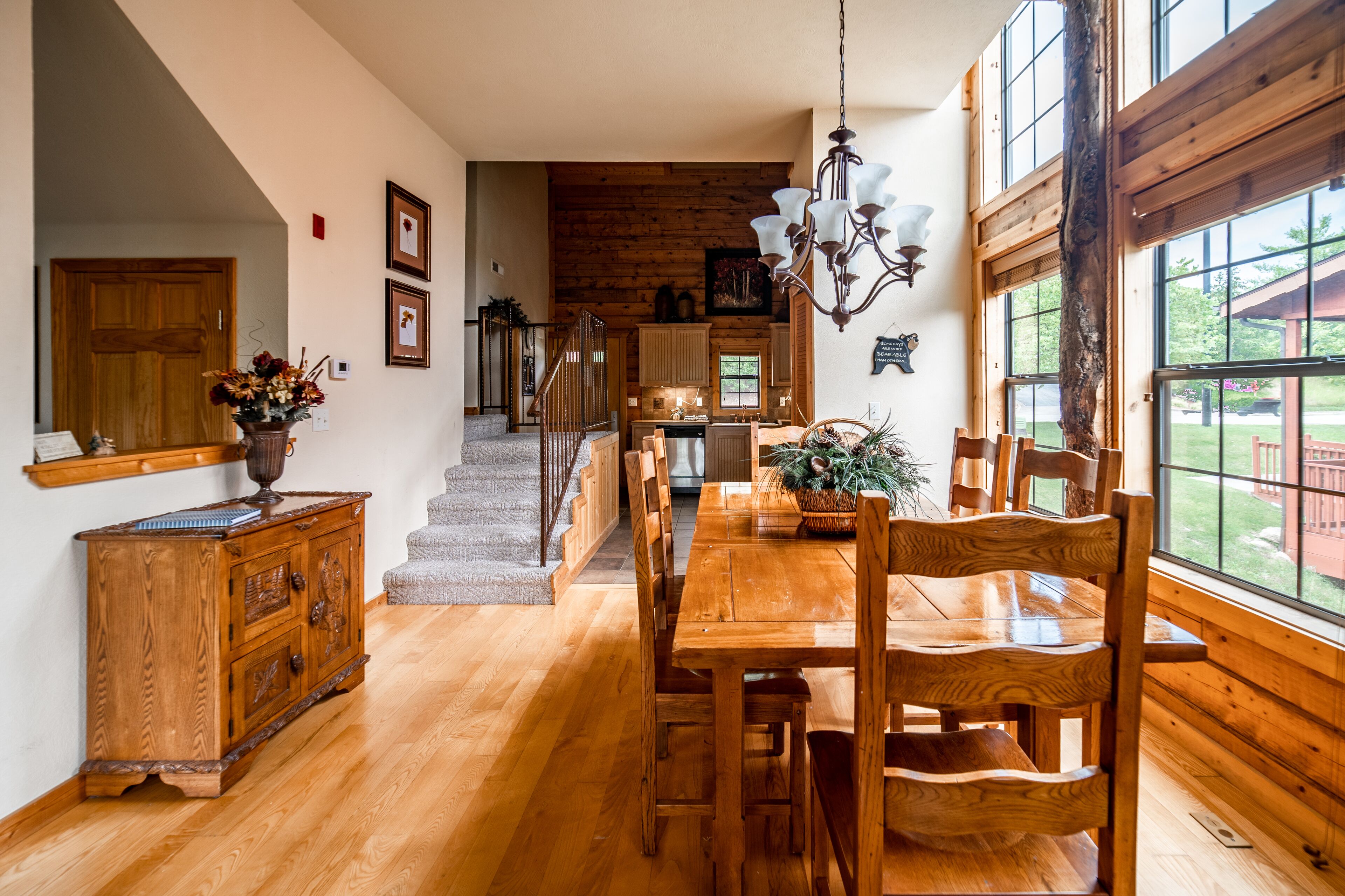 Un comedor amplio con una mesa y sillas de madera, una lámpara de araña y grandes ventanales que ofrecen vistas al exterior.