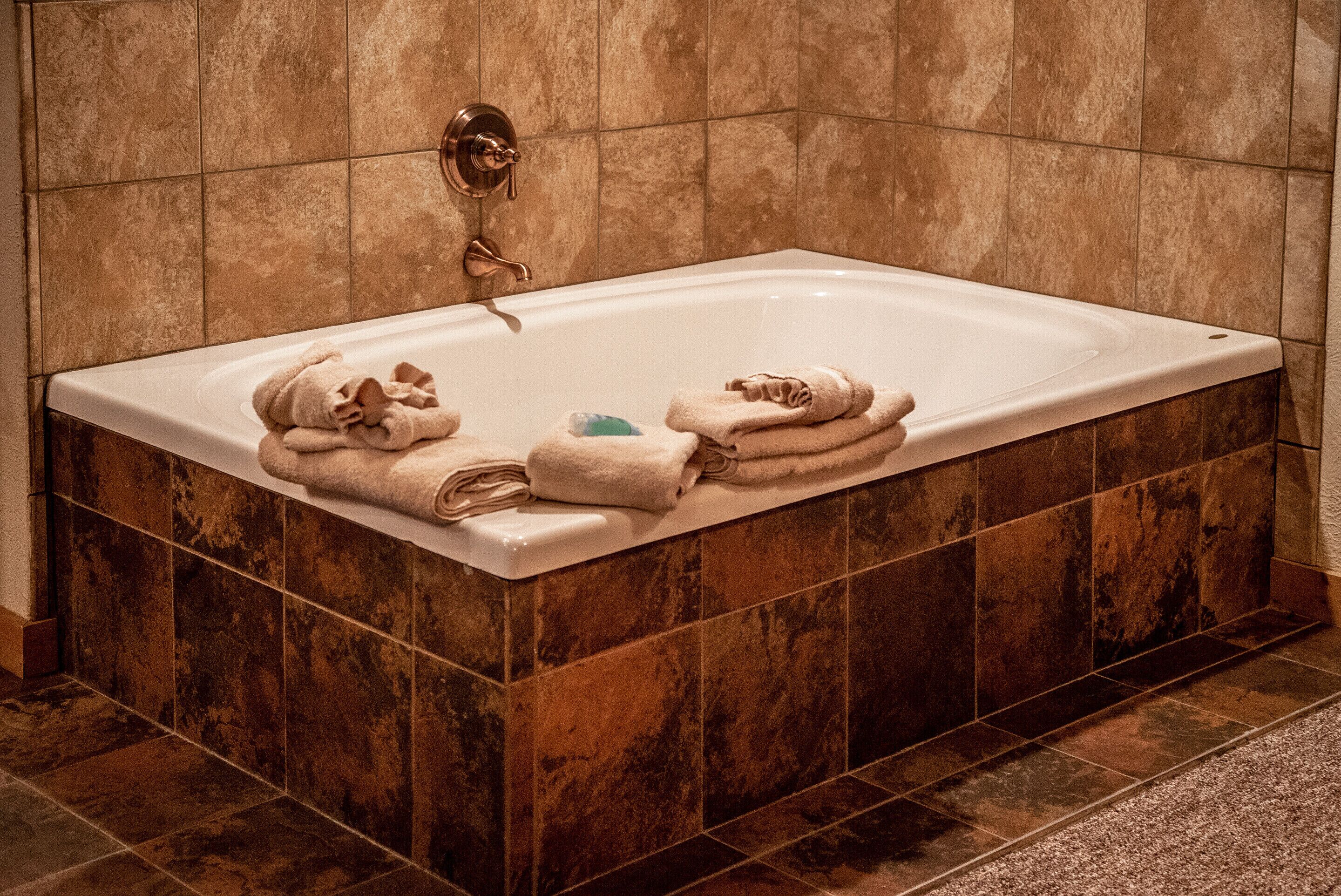 A rectangular bathtub with a faucet and a control knob, surrounded by brown tiles.