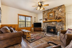 A cozy living room with a stone fireplace, wooden furniture, and a large window. - Cabins at Grand Mountain (Branson)