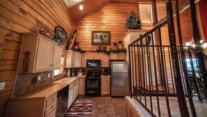 A log cabin-style kitchen with wooden walls, a stainless steel refrigerator, a microwave, and a stove. - Cabins at Grand Mountain (Branson)