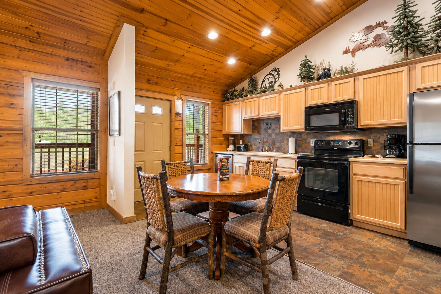 A wooden interior with a dining table, chairs, a kitchen with appliances, and a fireplace.