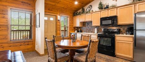 A wooden interior with a dining table, chairs, a kitchen with appliances, and a fireplace.