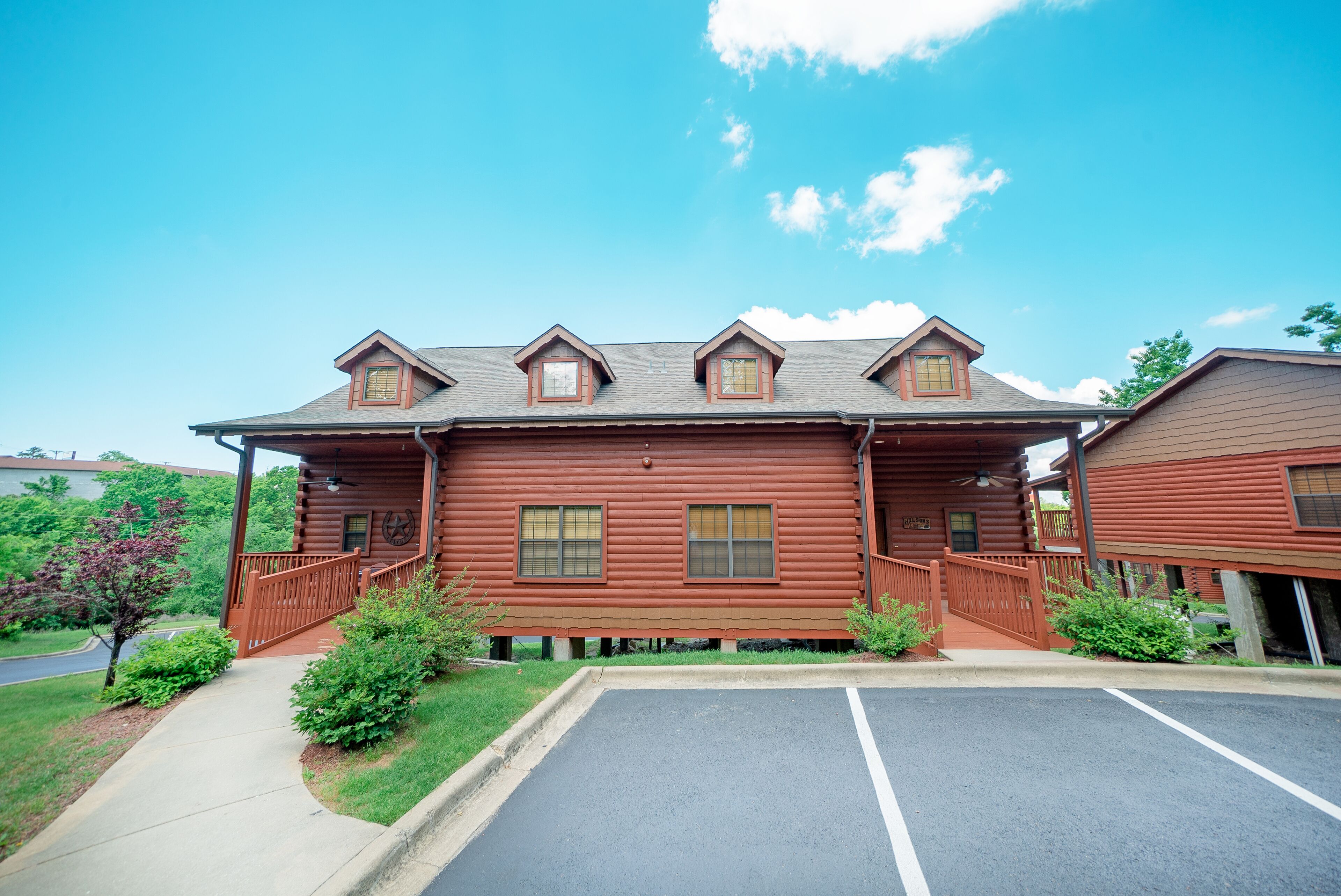 A two-story log cabin with a covered porch, a parking lot, and a clear blue sky.