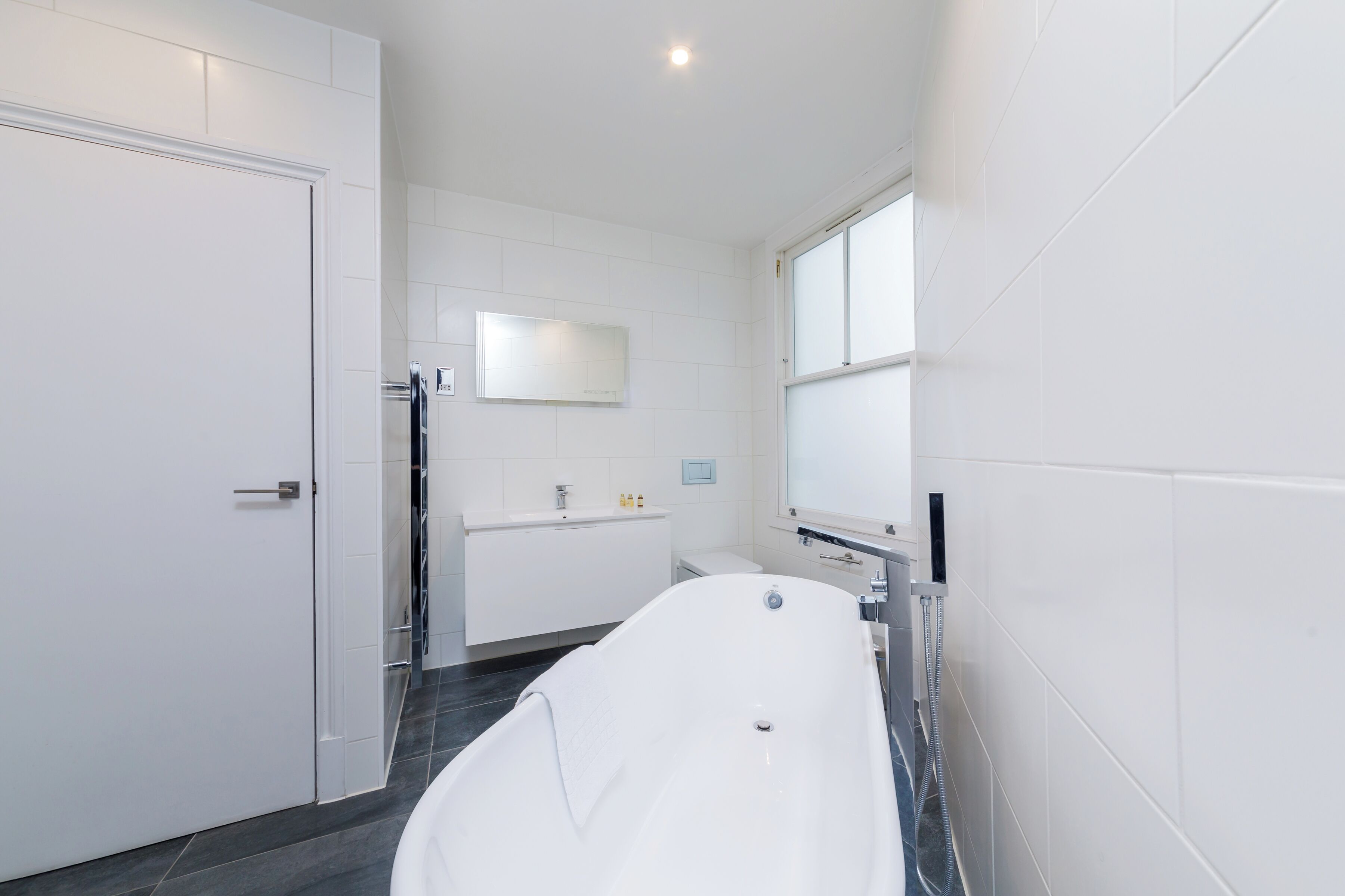 A modern bathroom with a freestanding bathtub, a vanity with a mirror, and a toilet.