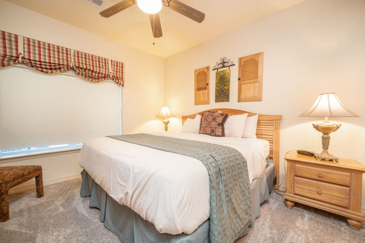 Un dormitorio con cama, mesitas de noche, un banco, ventilador de techo y adornos en la pared.