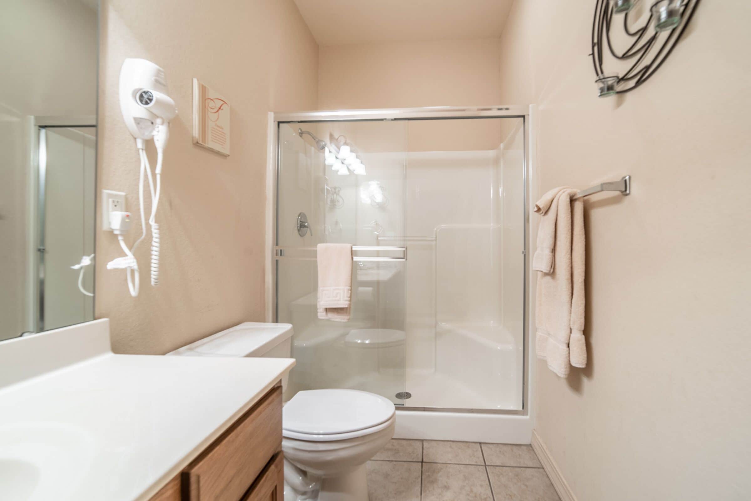 Un bagno con doccia vetrocamera, un water bianco, un asciugacapelli montato sulla parete e un portasciugamani.