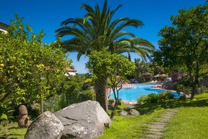A pool surrounded by lush greenery and palm trees, with a clear blue sky.