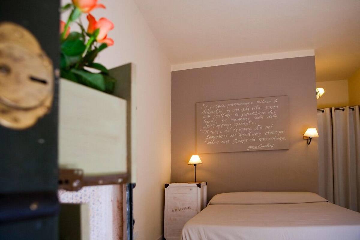 Une chambre d’hôtel avec un lit, une lampe fixée au mur, un mur orné d’une citation manuscrite et un arrangement floral.