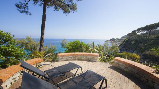 Une terrasse en bois avec deux chaises longues donnant sur une vue panoramique de la côte.