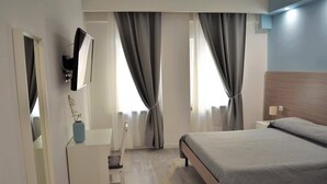 Una habitación de hotel moderna con una cama, un televisor montado en la pared, un tocador y un escritorio con una lámpara.
