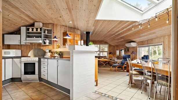 Eine moderne Küche mit weißen Schränken, einer Mikrowelle und einem Herd. Es gibt einen Essbereich mit Tisch und Stühlen, und ein großes Fenster sorgt für natürliches Licht.