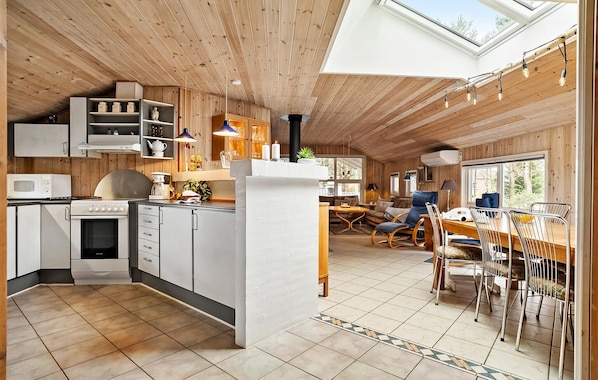 Une cuisine moderne avec des meubles blancs, un four à micro-ondes et une cuisinière. On y trouve un coin repas avec une table et des chaises, ainsi qu’une grande fenêtre qui laisse entrer la lumière naturelle.