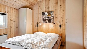 Ein Schlafzimmer mit Holzbalkendecke, einem Bett mit weißer Bettwäsche, einem an der Wand befestigten abstrakten Gemälde und zwei Wandleuchten.