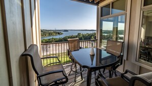 Ein Balkon mit Tisch und Stühlen mit Blick auf einen See und eine Brücke.