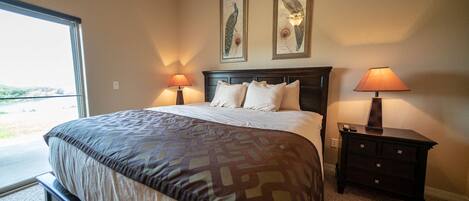 A bedroom with a large bed, two wall-mounted lamps, a nightstand, and two framed peacock pictures.