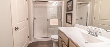 A bathroom with a glass shower enclosure, a toilet, a sink with a mirror, and a vanity with cabinets.