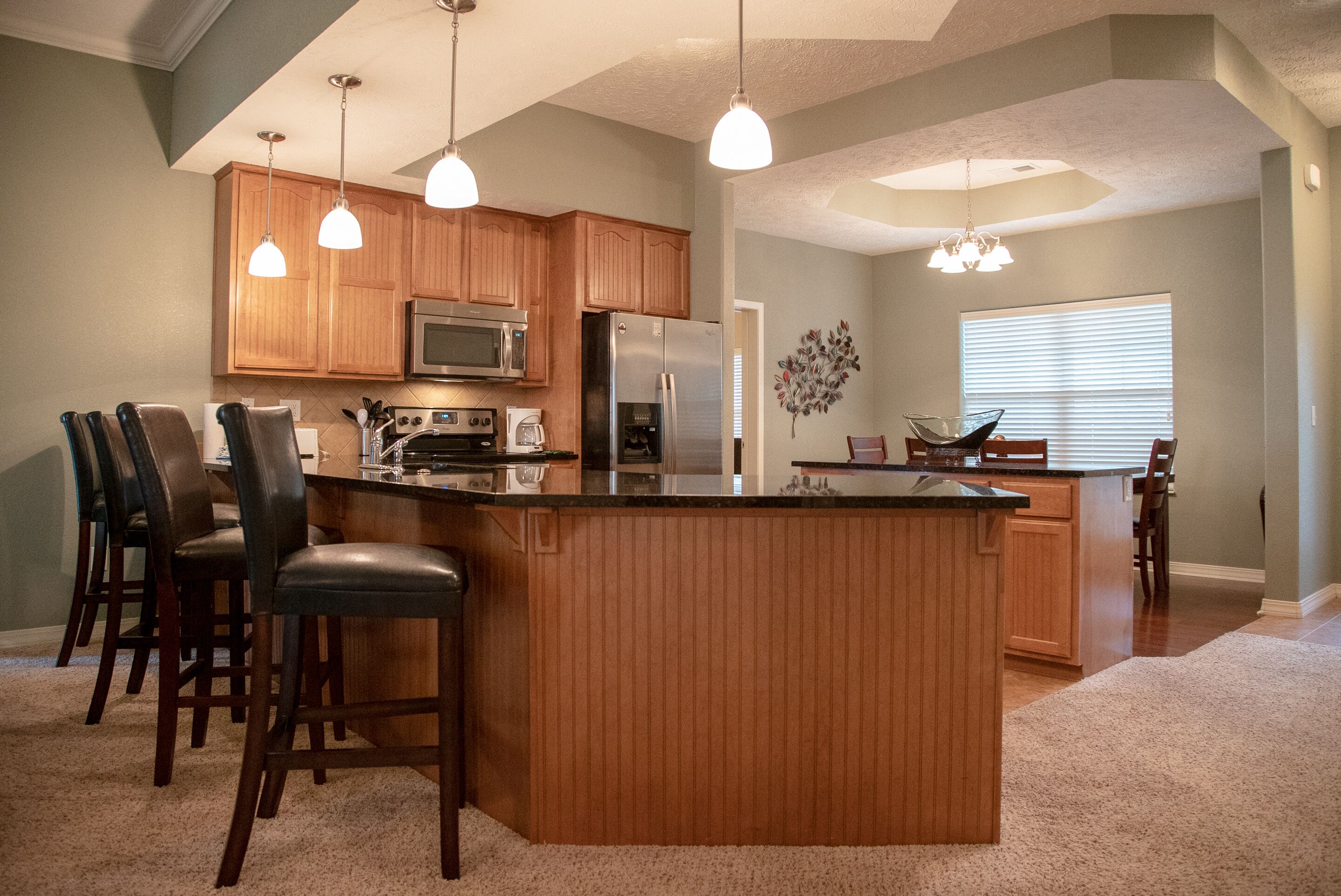 A kitchen with wooden cabinets, a central island with bar stools, a refrigerator, and a microwave.