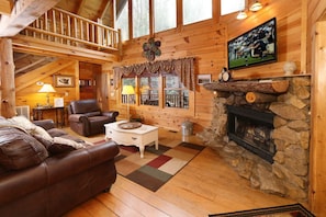 A cozy cabin interior with a fireplace, leather furniture, and a television.