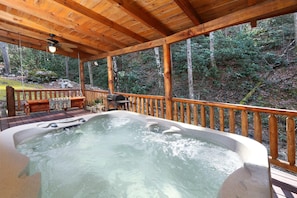 A hot tub in a wooden deck area with a wooden railing and a bench.