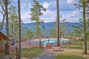 A pool area with a wooden deck, surrounded by trees and a mountain view.