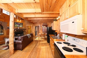 A cozy cabin interior with a living room, fireplace, dining area, and kitchen.