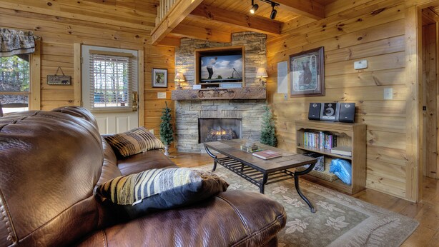 A cozy cabin interior with a stone fireplace, leather sofa, and a television mounted above it.