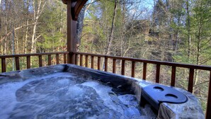A hot tub with a wooden deck and railing, surrounded by trees.
