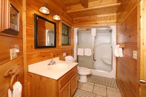A wooden cabin bathroom with a sink, toilet, and glass-enclosed shower.