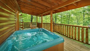 Una terraza de madera con un jacuzzi y barandas de madera que dan a un bosque.