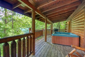 A wooden deck with a hot tub, surrounded by a wooden railing and a view of a forest. - American Treehouse #1708 (Sevierville)