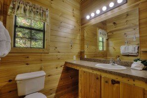 Baño de cabaña de madera con inodoro, lavamanos y espejo.