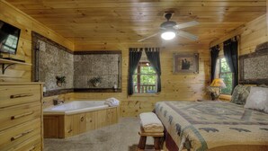 A wooden cabin room with a bed, a bathtub, a wooden dresser, and a ceiling fan. - A Beary Tale #258 (Sevierville)