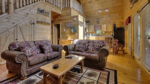 A log cabin interior with two sofas, a wooden table, and a staircase leading to an upper level. - A Beary Tale #258 (Sevierville)