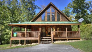 A wooden cabin with a green roof, a porch, and a sign indicating it is a campground. - A Beary Tale #258 (Sevierville)