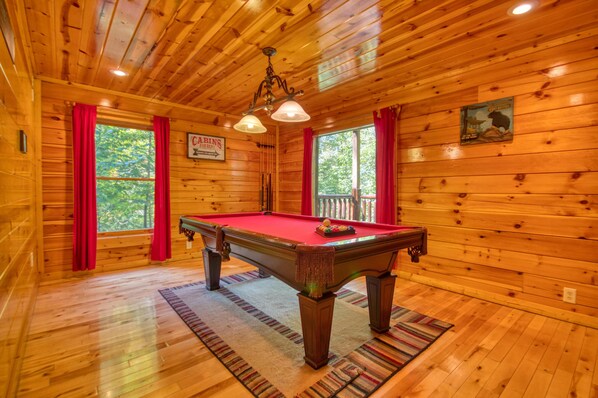 Una cabaña de madera con mesa de billar, cortinas rojas y un cartel que dice 'CABINS FOR RENT'.