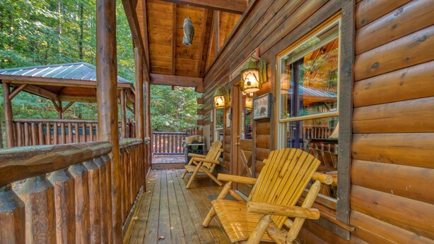 A wooden cabin with a porch, wooden deck, and a covered area with chairs and a table.