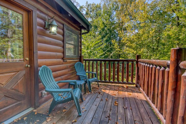 A wooden cabin with a porch, two Adirondack chairs, and a wooden railing. - Falcon Crest #2911 (Sevierville)