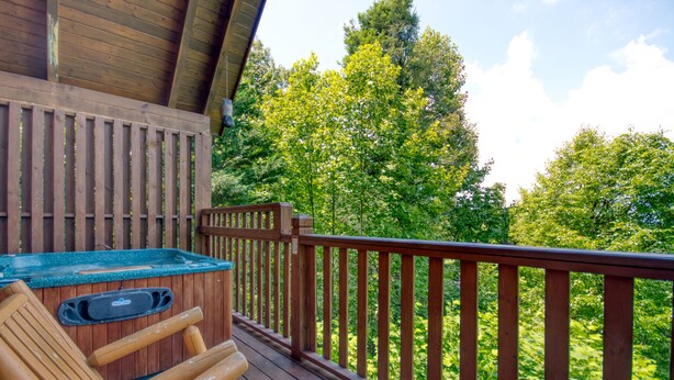A wooden deck with a hot tub and lounge chairs, overlooking a forested area. - American Dream #142 (Sevierville)