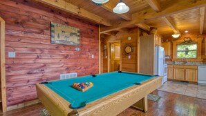 A wooden interior with a pool table, wooden cabinets, and a kitchen area. - American Dream #142 (Sevierville)