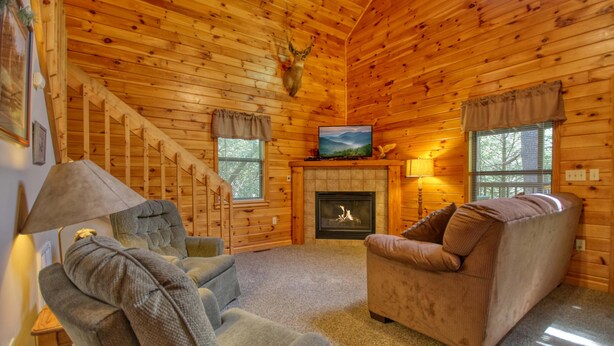 A log cabin interior with a fireplace, a television, and a cozy seating area.