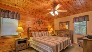 A bedroom with a wooden ceiling, a bed with striped bedding, two bedside tables with lamps, a dresser, and a chair.