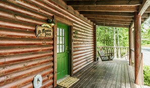 Une cabane en bois avec une porte verte, une pancarte de bienvenue et une véranda avec un banc.