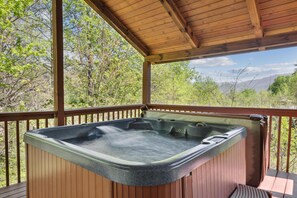 Un jacuzzi en una terraza de madera con vista a árboles y montañas.
