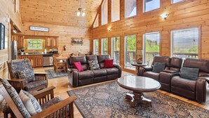 A spacious log cabin interior with a dining area, a leather sofa set, and a large window overlooking greenery. - Hillbilly Hilton #525 (Gatlinburg)