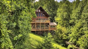 A two-story log cabin with a balcony, surrounded by dense forest. - Hillbilly Hilton #525 (Gatlinburg)
